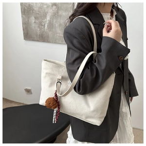 Detail of minimalist cream tote bag featuring CH print and cute brown teddy bear charm