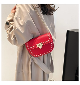 Detail of red lychee leather saddle bag with gold rivets and chain strap on trench coat