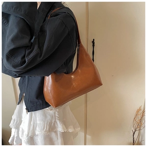 Detail of a brown leather shoulder bag featuring minimalist embossed logo and glossy texture