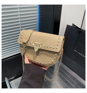 Detail of khaki saddle bag featuring golden rivets and elegant chain strap closeup