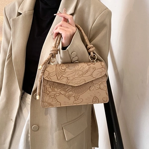 Detail of beige handbag featuring embossed lotus and koi fish patterns with a woven handle