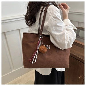 Detail view of a large brown suede tote bag with a plush bear charm on a female model