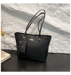 Detail of black pebbled leather tote bag with gold metal plate and mini hanging pouch