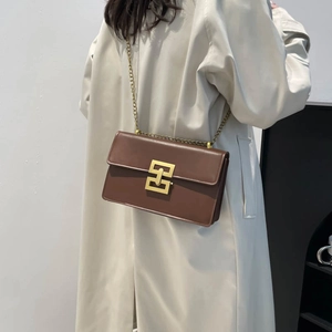 Brown leather crossbody bag with gold chain strap and square buckle on beige trench coat