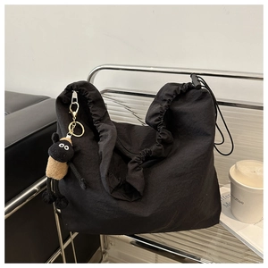 Detail of black nylon tote bag with drawstring closure and a sheep plush pendant on a chair