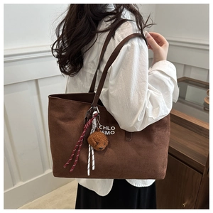 Brown suede tote bag detail featuring white text and a teddy bear plush charm accessory