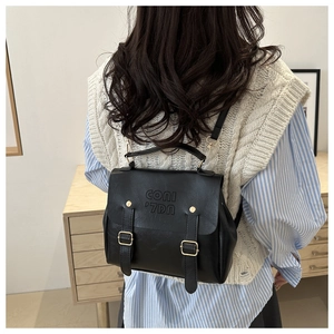 Minimalist black leather backpack with flap design and gold buckles worn by a model