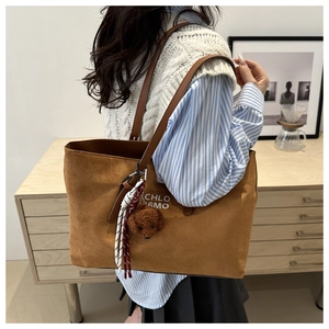 Detail of brown suede tote bag with leather straps and plush puppy charm in home setting