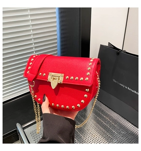 Detail of red pebbled leather saddle bag with gold rivets and metallic chain strap