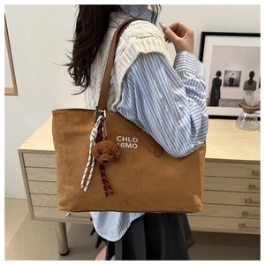 Brown suede tote bag with decorative plush charm and white lettering on shoulder strap