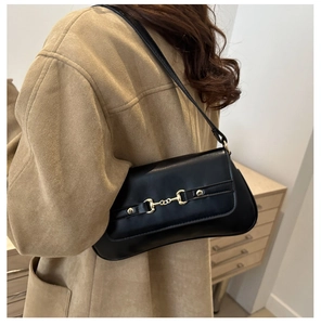Détail du sac baguette en cuir noir avec boucle mors dorée porté sur un manteau beige