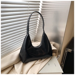 Close-up of minimalist black glossy leather crescent bag on cream fabric with striped shadows