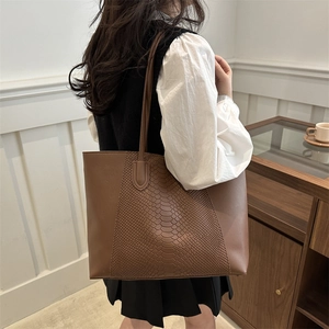 Brown tote bag in smooth leather and snake pattern worn by a model in a cozy cafe