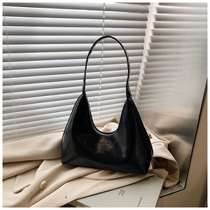 Detail of a black crescent hobo bag made of glossy leather on a beige trench coat
