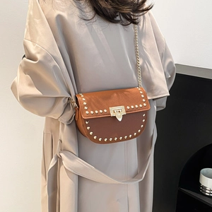 Brown litchi leather saddle bag with gold rivets and chain strap on beige trench coat
