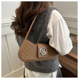 Sac sous le bras marron à monogramme avec logo M argenté porté dans un cadre minimaliste