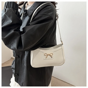 Side view of model wearing a beige crescent underarm bag with a golden bow buckle