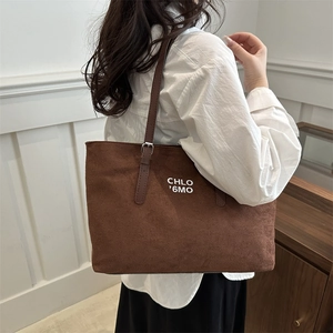 Brown suede tote bag with white lettering and leather straps shown on a female model