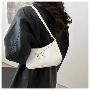 Detailed view of a white crescent underarm bag with a golden metal bow on a model