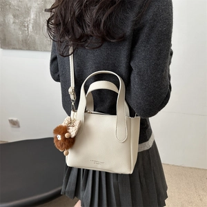 Minimalist beige pebble leather bucket bag with plush charm and crossbody strap