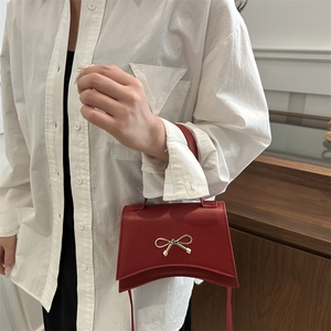Red crossbody mini bag with golden bow clasp and curved bottom on model in a home setting