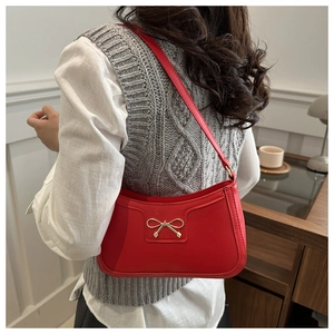 Detail of red crescent shoulder bag featuring a polished gold bow buckle and leather stitching