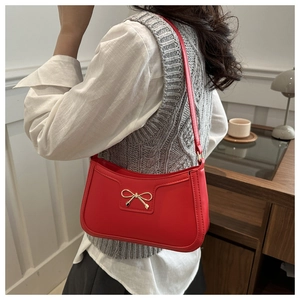 Detailed view of red crescent shoulder bag with golden bow hardware on model
