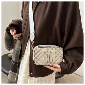 Détail du sac caméra rectangulaire blanc cassé avec monogramme et logo SM en métal