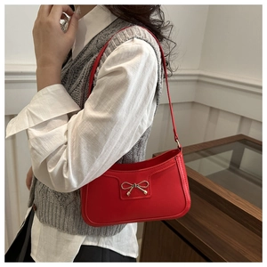 Macro detail of red crescent shoulder bag featuring a decorative gold metal bow accent