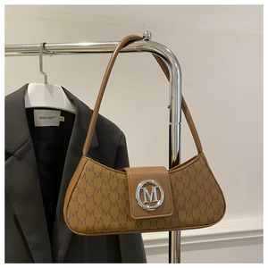 Gros plan détaillé du motif monogramme marron et du logo M sur un sac baguette porté épaule