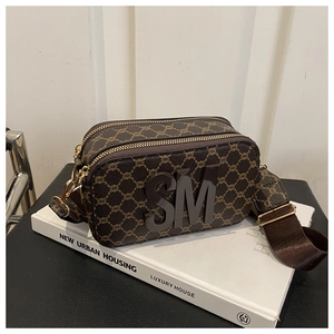 Gros plan du sac caméra marron avec motif géométrique et bandoulière sur des livres