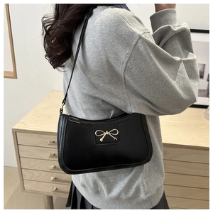 Close-up of black leather crescent bag featuring a delicate golden metal bow detail