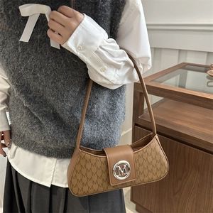 Sac baguette marron avec monogramme et boucle M, porté sur un gilet gris et une chemise blanche