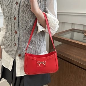 Chic red crescent underarm bag with gold bow detail, styled on model for a trendy look
