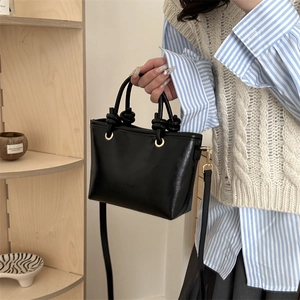 Chic black matte bucket bag with knot handle detail and gold hardware for 2025 fashion