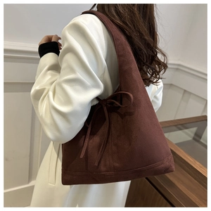 Detail of dark brown suede tote bag featuring a decorative side bow on a female model