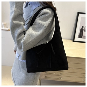 Close-up of black suede tote bag with decorative bow detail in a minimalist setting