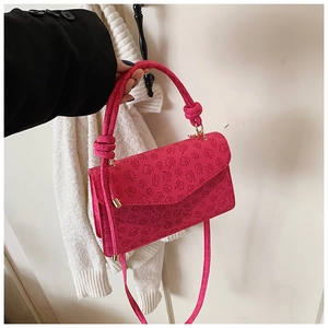 Detail of rose red crossbody bag featuring embossed clover patterns and knotted handle