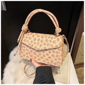 Close-up of cream square bag with embossed clover pattern and knotted handle detail