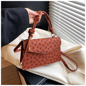 Close-up of brown square flap handbag featuring embossed floral patterns and knot handle