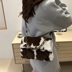 Borsa a tracolla in peluche a macchie di mucca marroni con catena, indossata da una modella