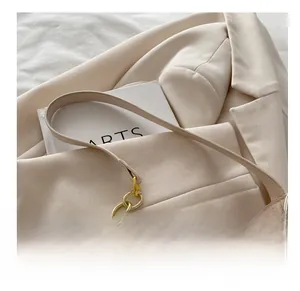 Détail du sac croissant beige avec chaîne dorée et texture en cuir lisse sur une veste