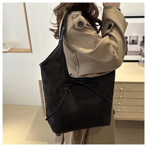 Detail of minimalist black suede tote bag with elegant bow detail on a stylish model