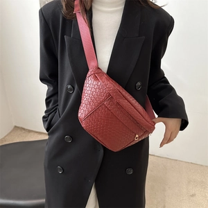 Deep red woven crossbody chest bag with gold zipper detail on a black blazer model
