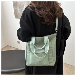 Sage green nylon tote bag shown on a model featuring a front pocket and crossbody strap