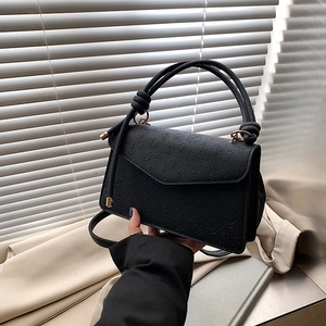 Detail of four-leaf clover embossing on black faux leather handbag with knot handle