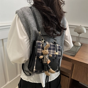 Retro plaid backpack with black leather trim and cute bunny charm in cozy home setting