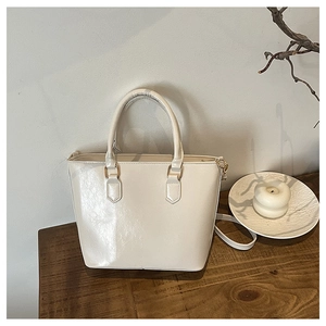 Détail du sac cabas crème brillant avec boucles métalliques dorées sur table en bois