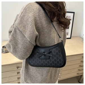 Detail of black monogram shoulder bag with bow accent worn by model in cozy home setting