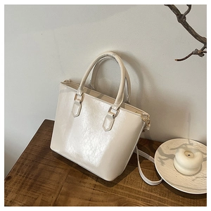Détail d'un sac seau en cuir verni crème avec boucles dorées sur une table en bois